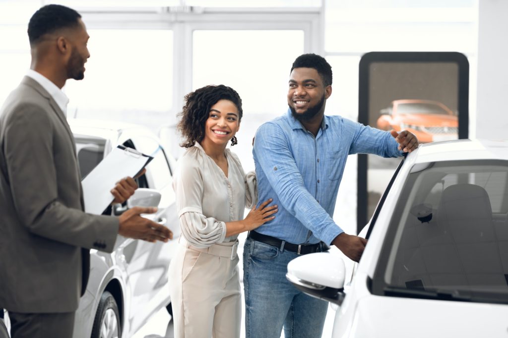 Couple Choosing Automobile With Professional Dealer In Luxury Dealership Store
